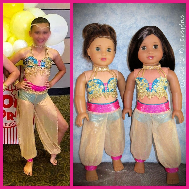 May include: Two dolls wearing matching turquoise, gold, and pink costumes. The costumes feature a jeweled top, a pink sash, and sheer gold pants. The dolls have brown hair and are standing on a light wood floor.