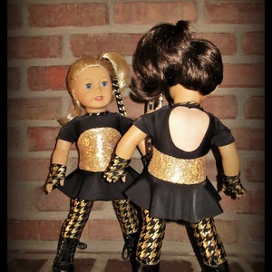 May include: Two dolls wearing black and gold dance costumes with black and white patterned leggings. The dolls are standing in front of a brick wall. The text "Janie carroll Designs" is visible at the bottom of the image.