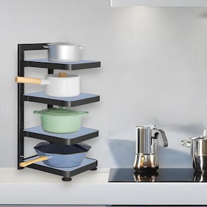 Puede incluir: Un estante esquinero de metal negro con cuatro niveles, cada uno con una pieza diferente de utensilios de cocina. Los utensilios de cocina incluyen una olla plateada, una olla blanca, una olla verde y una sartén azul. El estante está contra una pared gris claro.