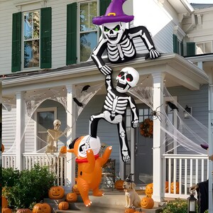 Peut inclure: Une décoration gonflable d'Halloween représentant un squelette portant un chapeau de sorcière violet sur un toit, tendant la main pour soulever un autre squelette. En bas, un chat gonflable orange à collier rouge se tient sur les marches.
