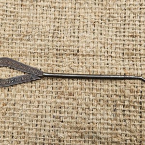 May include: A vintage metal shoe hook with a looped handle and a curved hook end. The handle is marked with the text "BOSTON STORE SHOES" and "N.H.K. CON. ST. MAIN."