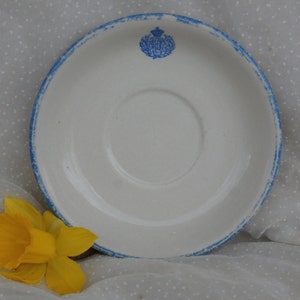 May include: White ceramic saucer with a blue rim and a blue and white crest in the center.