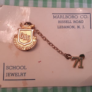 May include: Gold-colored school jewelry set with a pendant featuring the letters "GHS" inside a shield with the words "Student Council" around it, and a separate pendant with the number "71". The jewelry is on a white card with the text "MARLBORO CO. BISSELL ROAD LEBANON, N. J. SCHOOL JEWELRY".