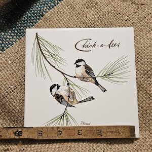 May include: Square ceramic tile featuring two chickadees perched on a pine branch. The birds are depicted in shades of brown, black, and white against a white background. The text "Chick-a-dees" is written in brown script. Signed "P. Howard".