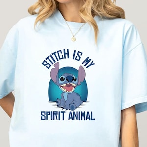 Puede incluir: Camiseta azul claro con una imagen de dibujos animados de Stitch y el texto "Stitch is my Spirit Animal". El gr&aacute;fico muestra a Stitch sonriendo con un fondo azul. Es una prenda informal.