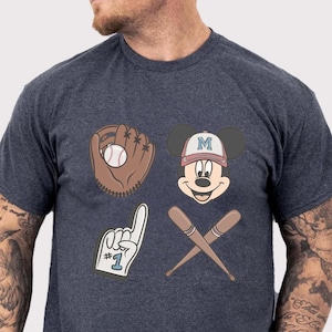 May include: Dark heather gray t-shirt featuring baseball-themed graphics. The design includes a baseball glove with a ball, Mickey Mouse wearing a baseball cap, crossed baseball bats, and a foam finger.