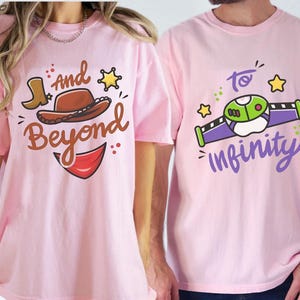 May include: Two light pink t-shirts. One shirt has a cartoon cowboy hat and boot with the words "And Beyond". The other shirt has a cartoon spaceship with the words "To Infinity".