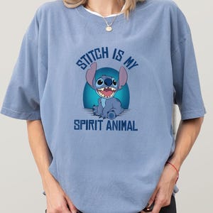 Puede incluir: Camiseta azul claro con un dise&ntilde;o de Stitch, el personaje de Disney. El texto "Stitch is my Spirit Animal" est&aacute; impreso encima y debajo de la imagen. La camiseta tiene mangas cortas y un corte holgado.