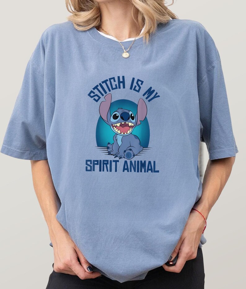 Puede incluir: Camiseta azul claro con un dise&ntilde;o de Stitch, el personaje de Disney. El texto "Stitch is my Spirit Animal" est&aacute; impreso encima y debajo de la imagen. La camiseta tiene mangas cortas y un corte holgado.