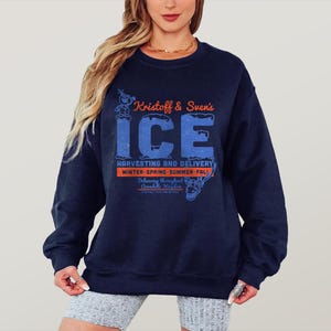 May include: A navy blue sweatshirt with the text "Kristoff & Sven's ICE" in orange and blue. The sweatshirt features a graphic of a cartoon character and the words "Harvesting and Delivery" and "Winter-Spring-Summer-Fall".