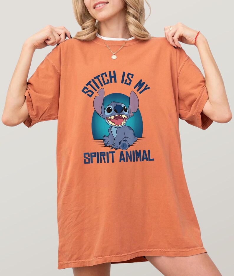 Puede incluir: Camiseta naranja con el personaje Stitch de Lilo & Stitch. El gr&aacute;fico azul muestra a Stitch con el texto "Stitch is my spirit animal" en azul. La camiseta es de color naranja liso.