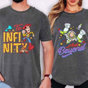 May include: Two charcoal grey t-shirts with Toy Story graphics. One shirt features Woody with the text "To Infinity" in yellow and "Nity" in orange. The other shirt has Buzz Lightyear with the text "And Beyond" in purple.