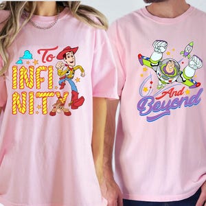 May include: Two light pink t-shirts with cartoon character designs. One features Woody with the words "To Infinity". The other shows Buzz Lightyear with the words "And Beyond". Both shirts have short sleeves.