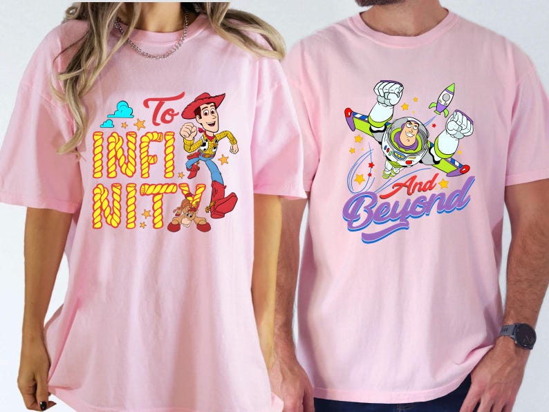 May include: Two light pink t-shirts with cartoon character designs. One features Woody with the words "To Infinity". The other shows Buzz Lightyear with the words "And Beyond". Both shirts have short sleeves.