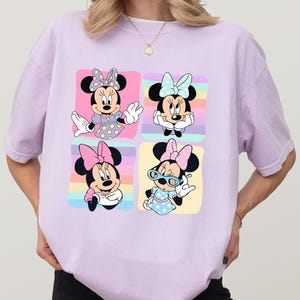 Może przedstawiać: Jasnofioletowa koszulka z czteropanelową grafiką Myszki Minnie w r&oacute;żnych pozach. Każdy panel ma inny kolor tła, a Myszka Minnie ma na sobie inną kokardę i str&oacute;j w każdym panelu.