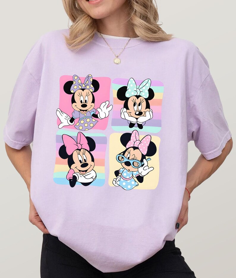 Może przedstawiać: Jasnofioletowa koszulka z czteropanelową grafiką Myszki Minnie w r&oacute;żnych pozach. Każdy panel ma inny kolor tła, a Myszka Minnie ma na sobie inną kokardę i str&oacute;j w każdym panelu.
