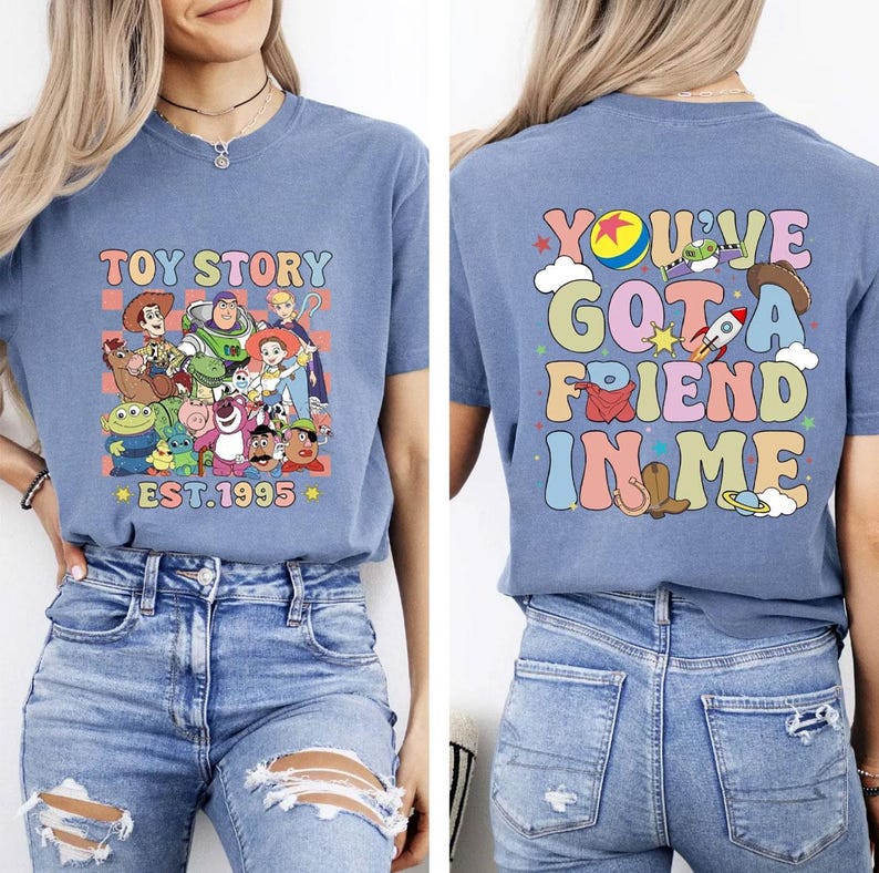 May include: A light blue t-shirt featuring a colorful graphic of Toy Story characters with the text "TOY STORY EST.1995" on the front. The back of the shirt displays the phrase "YOU'VE GOT A FRIEND IN ME" with related graphics.