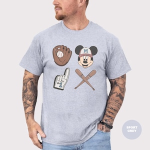 May include: Sport grey t-shirt featuring baseball-themed graphics. The design includes a baseball glove with a ball, Mickey Mouse wearing a baseball cap, crossed bats, and a foam finger. The shirt is a light grey color.