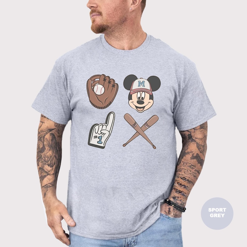 May include: Sport grey t-shirt featuring baseball-themed graphics. The design includes a baseball glove with a ball, Mickey Mouse wearing a baseball cap, crossed bats, and a foam finger. The shirt is a light grey color.