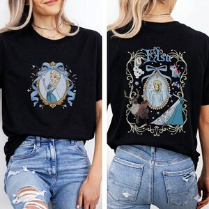 May include: Black t-shirt featuring a front and back design. The front displays a framed image of a blonde woman in a blue dress, with blue ribbons. The back features the name "Elsa" and a similar framed image with other characters.