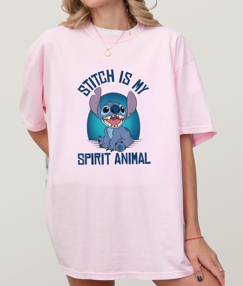 Puede incluir: Camiseta rosa claro con una imagen de dibujos animados de Stitch de Lilo & Stitch. El personaje azul de Stitch sonr&iacute;e, con el texto "Stitch is my Spirit Animal" en letras azules. La camiseta es de estilo casual y oversize.