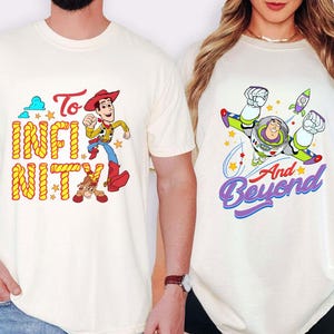 May include: Two cream-coloured t-shirts. One features Woody with the text "To Infinity" in yellow and orange. The other shirt displays Buzz Lightyear with the text "And Beyond" in purple and blue, with a rocket and stars.