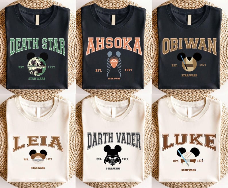 Op de afbeelding: Zes T-shirts met Star Wars-ontwerpen. De shirts tonen de namen "Death Star", "Ahsoka", "Obiwan", "Leia", "Darth Vader" en "Luke" in een collegiale lettertype, samen met het jaar "1977" en het Star Wars-logo. Elk ontwerp bevat een Mickey Mouse silhouet.