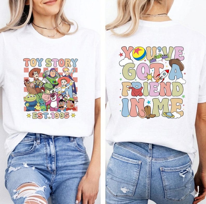 May include: White t-shirt featuring a colorful graphic of Toy Story characters with the text "TOY STORY EST.1995" on the front. The back of the shirt displays the phrase "YOU'VE GOT A FRIEND IN ME" with various Toy Story themed illustrations.