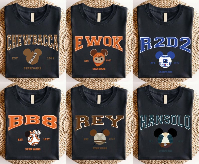 Op de afbeelding: Zes zwarte t-shirts met Star Wars-personagenamen in collegiale letters. Elk shirt heeft de naam van een personage, een op Mickey Mouse ge&iuml;nspireerde afbeelding en de tekst "EST. 1977 STAR WARS". Personages zijn onder meer Chewbacca, Ewok, R2D2, BB8, Rey en Han Solo.