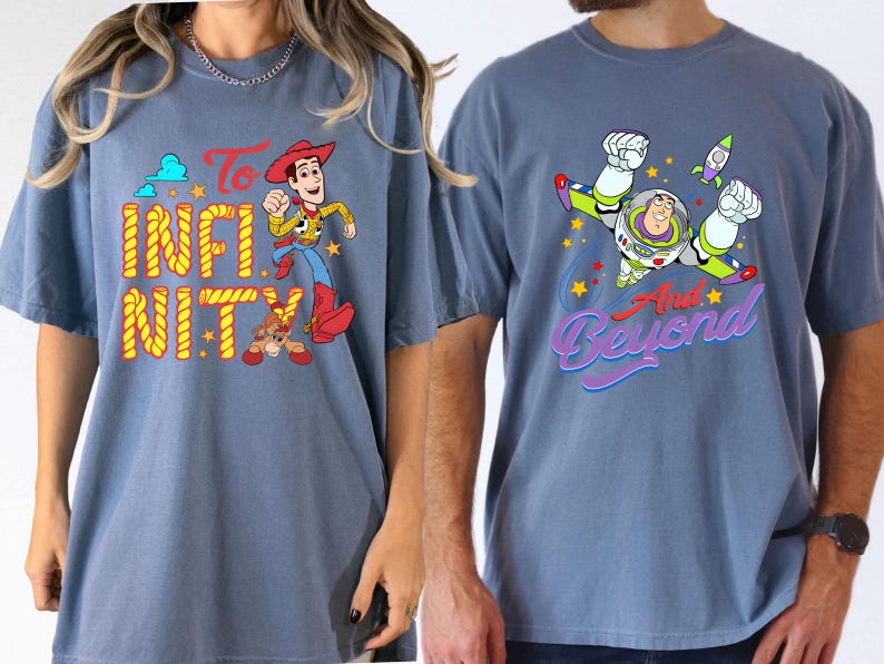 May include: Two blue t-shirts featuring characters from Toy Story. One shirt displays Woody with the words "To Infinity", the other Buzz Lightyear with "And Beyond". Both shirts have colourful graphics.