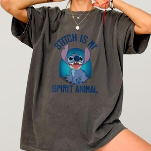 Puede incluir: Camiseta gris oscuro con un personaje de dibujos animados azul y el texto "Stitch is my Spirit Animal". El personaje est&aacute; sobre un fondo azul. La camiseta tiene mangas cortas y un corte holgado.