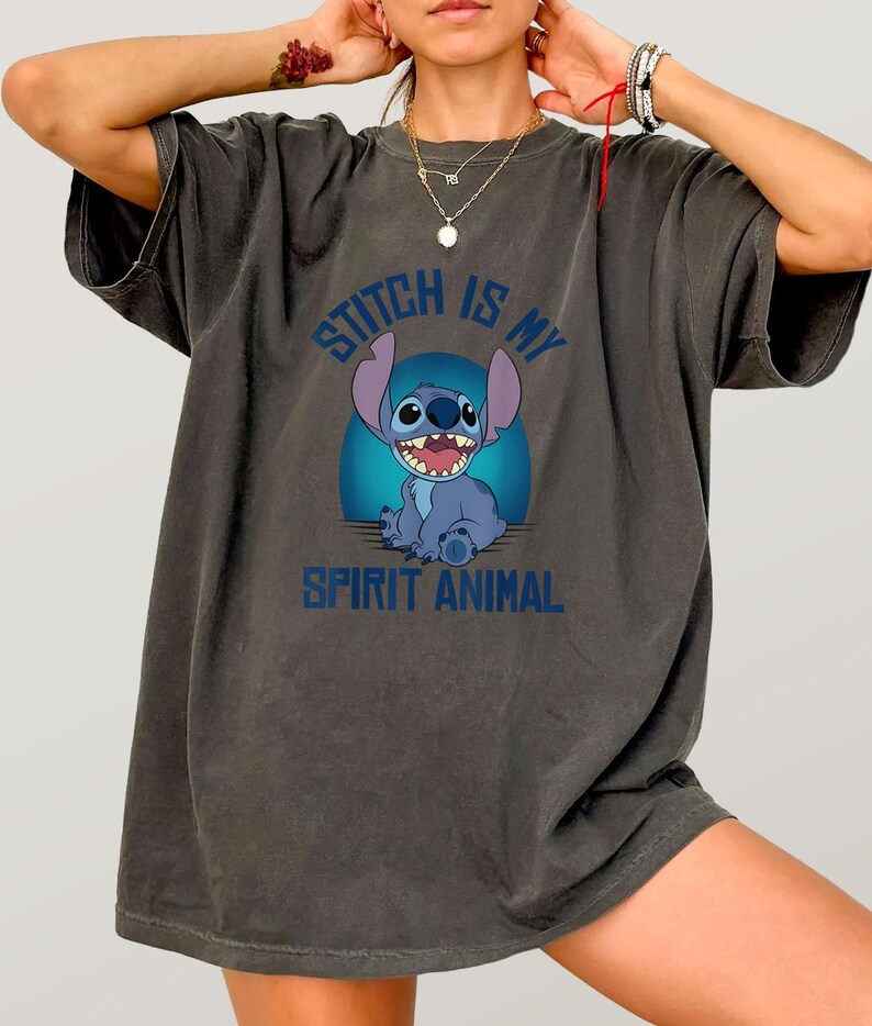 Puede incluir: Camiseta gris oscuro con un personaje de dibujos animados azul y el texto "Stitch is my Spirit Animal". El personaje est&aacute; sobre un fondo azul. La camiseta tiene mangas cortas y un corte holgado.
