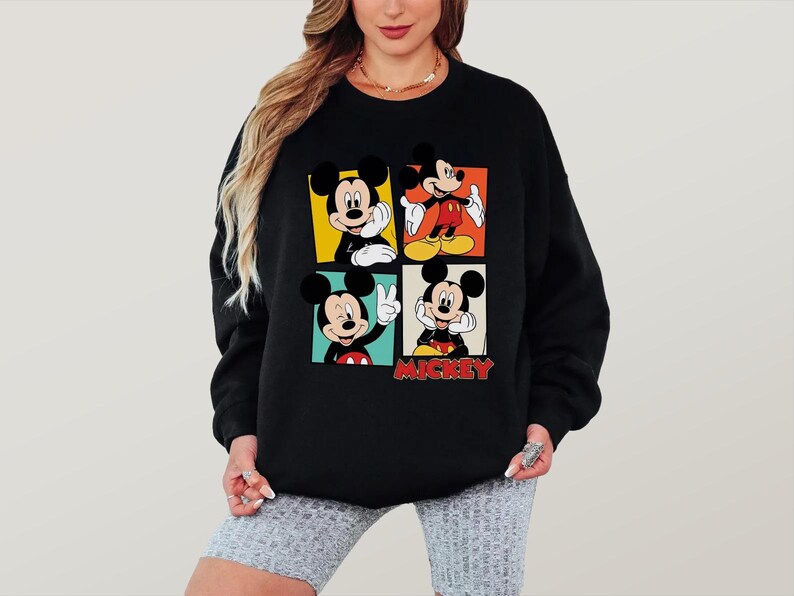 Peut inclure: Sweat-shirt noir avec quatre panneaux repr&eacute;sentant Mickey Mouse dans diff&eacute;rentes poses. Chaque panneau a un fond de couleur diff&eacute;rente : jaune, orange, rouge et vert. Le mot "Mickey" est en lettres rouges en bas.
