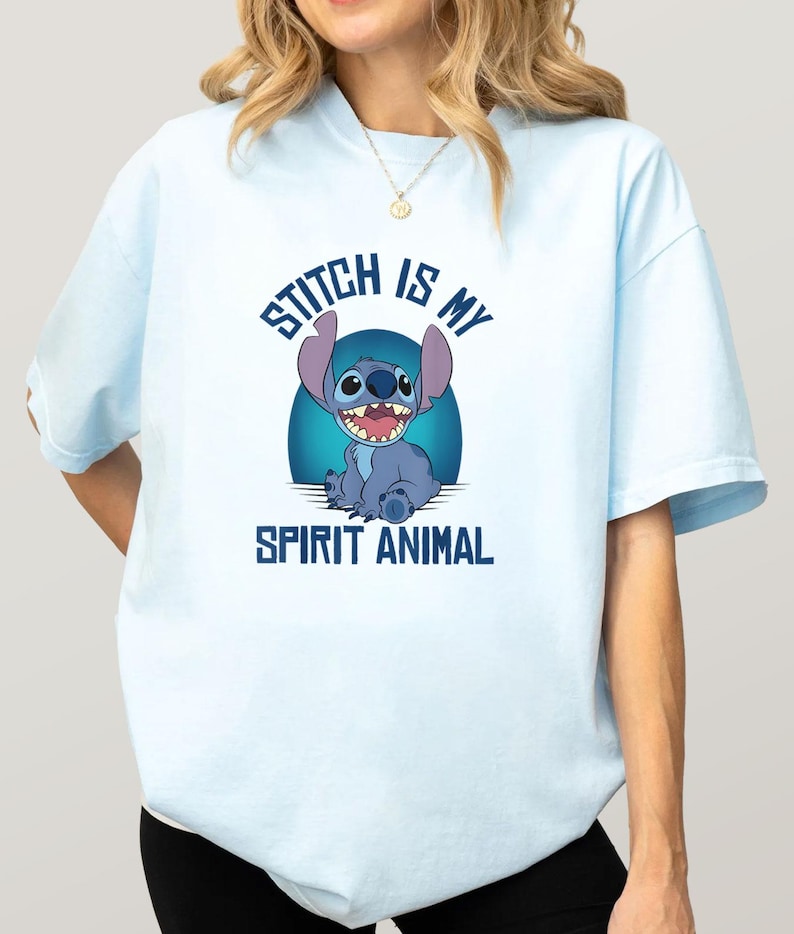Puede incluir: Camiseta azul claro con una imagen de dibujos animados de Stitch y el texto "Stitch is my Spirit Animal". El gr&aacute;fico muestra a Stitch sonriendo con un fondo azul. Es una prenda informal.
