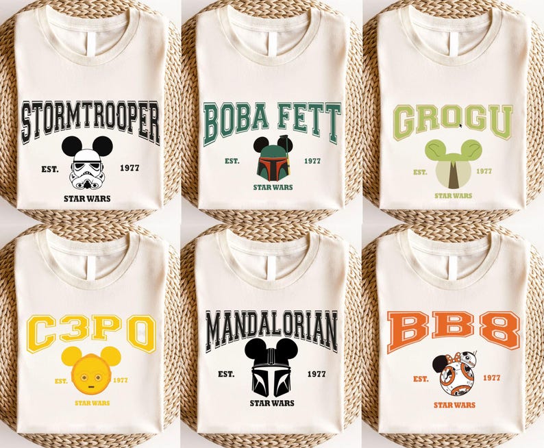 Op de afbeelding: Cr&egrave;mekleurige T-shirts met Star Wars-personages: Stormtrooper, Boba Fett, Grogu, C3PO, Mandalorian en BB8. Elk shirt heeft een personagenaam in een universiteitslettertype, een Mickey Mouse-hoofd en de tekst "EST. 1977 STAR WARS."