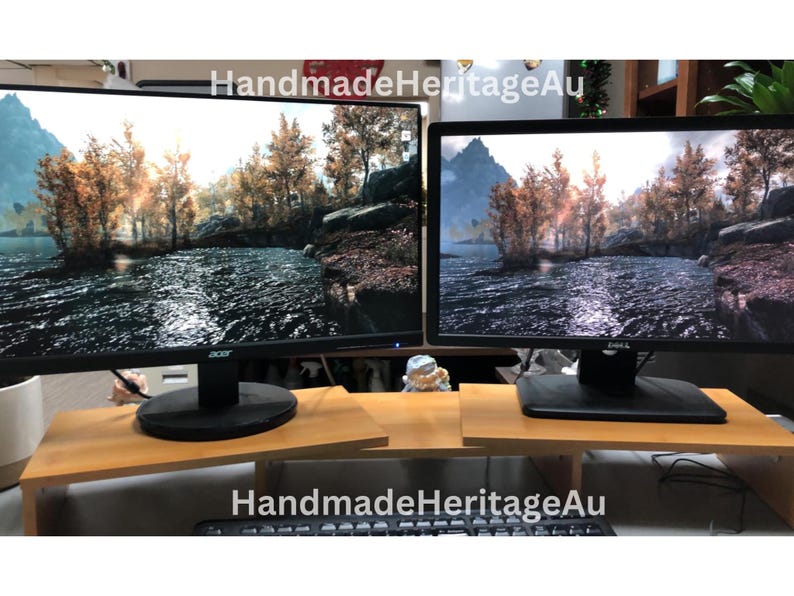May include: Two computer monitors displaying a scenic landscape are placed on a light brown wooden monitor stand. The stand has a keyboard shelf. The text "HandmadeHeritageAu" is visible on the image.