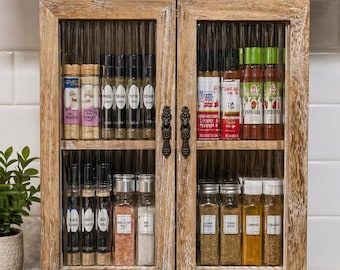 May include: A wooden spice rack with two glass doors, filled with spice jars. The rack is made of light-coloured wood and has decorative handles. The jars contain herbs and spices like thyme, basil, and paprika. The cabinet is approximately 40 cm wide.