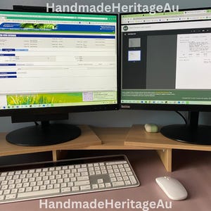 May include: A dual monitor setup with a light wood-tone monitor stand. A white keyboard and mouse are on the desk. The monitors display website content. The text "HandmadeHeritageAu" is at the bottom of the image.