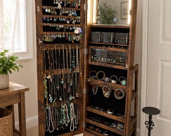 May include: A tall, wooden jewelry armoire with a full-length mirror and interior LED lighting. The open door reveals numerous hooks and compartments for necklaces, earrings, bracelets, and rings. The armoire is a dark brown colour.