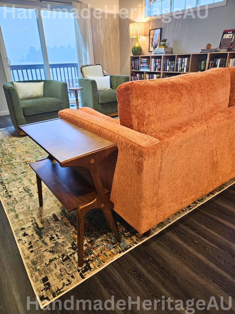 K&ouml;nnte beinhalten: Ein Wohnzimmer im Mid-Century-Modern-Stil mit einem orangefarbenen Sofa, zwei gr&uuml;nen Sesseln und einem Beistelltisch aus Holz. Ein gemusterter Teppich und dunkler Holzboden vervollst&auml;ndigen den Raum. Der Raum ist gut beleuchtet.