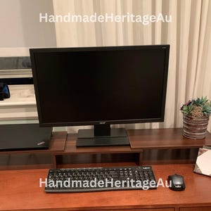 May include: A dark brown wooden desk with a computer monitor, keyboard, and mouse. A laptop sits on a lower shelf. A small potted plant and a notepad are also on the desk. The text "HandmadeHeritageAu" is in the top left corner.