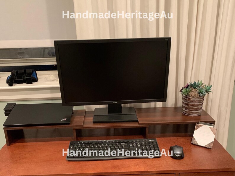 May include: A dark brown wooden desk with a computer monitor, keyboard, and mouse. A laptop sits on a lower shelf. A small potted plant and a notepad are also on the desk. The text "HandmadeHeritageAu" is in the top left corner.