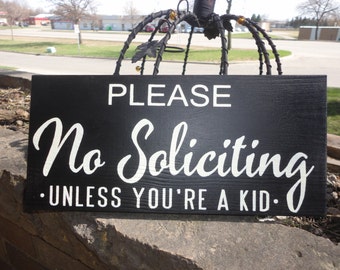 May include: Black wooden sign with white text that reads "PLEASE No Soliciting - UNLESS YOU'RE A KID."