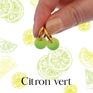 Peut inclure: Boucles d'oreilles créoles dorées avec de petites perles rondes vert clair. Les boucles d'oreilles sont présentées sur un fond blanc avec un motif de tranches de citron vert et le texte "Citron vert".
