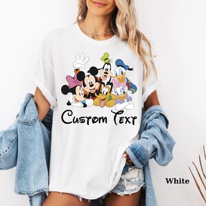 May include: White t-shirt with a colourful graphic of Disney characters such as Mickey and Minnie Mouse, Goofy, Donald and Daisy Duck, and Pluto. The words "Custom Text" are printed in black script. The word "White" is printed in black.