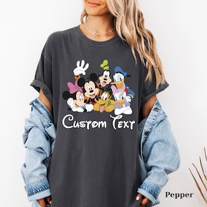 May include: Dark grey t-shirt with a colourful graphic of Disney characters, including Mickey and Minnie Mouse, Goofy, Donald and Daisy Duck, and Pluto. The words "Custom Text" are written in white script below.