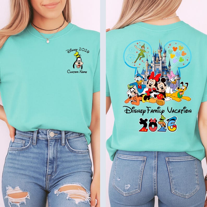 Op de afbeelding: Een lichtblauwgroen T-shirt met Disney-personages. De voorkant heeft een Goofy-afbeelding en de tekst "Disney 2026" en "Custom Name". De achterkant heeft een Disney-kasteelafbeelding, de tekst "Disney Family Vacation 2026" en andere Disney-personages.