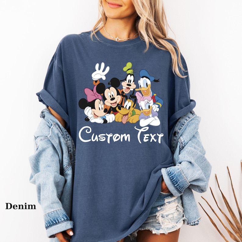 May include: A navy blue t-shirt with a graphic of Mickey Mouse, Minnie Mouse, Goofy, Pluto, Donald Duck, and Daisy Duck. The words "Custom Text" are written in white script below the characters. The word "Denim" is written in the bottom left corner.