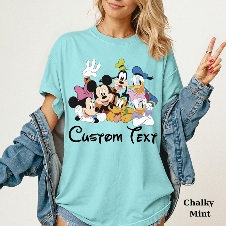 May include: A light blue t-shirt with a graphic of Disney characters: Mickey, Minnie, Goofy, Donald, Daisy, and Pluto. The text "Custom Text" is printed below the characters. The words "Chalky Mint" are printed at the bottom right.