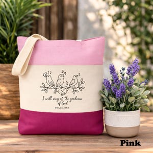 May include: A pink and cream tote bag with a cream-colored handle. The bag features a design of three singing birds on a branch, with the text "I will sing of the goodness of God" and "Psalm 89:1".